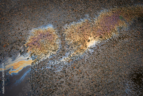A spot of oil or gasoline in a puddle on the asphalt. Top view of asphalt with oil after rain