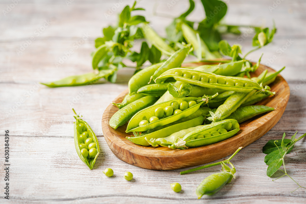 Fresh green peas in wooden bowl with pods and leaves on white wooden table, healthy green vegetable or legume Fresh green peas in wooden bowl with pods and leaves on white wooden table, healthy green vegetable or legume