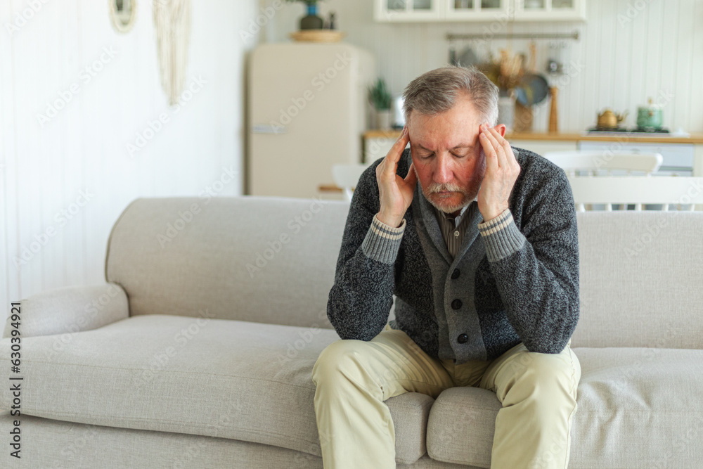 Headache pain. Unhappy middle aged senior man suffering from headache sick rubbing temples at home. Mature old senior grandfather touching temples experiencing stress. Man feeling pain hurt in head Headache pain. Unhappy middle aged senior man suffering from headache sick rubbing temples at home. Mature old senior grandfather touching temples experiencing stress. Man feeling pain hurt in head