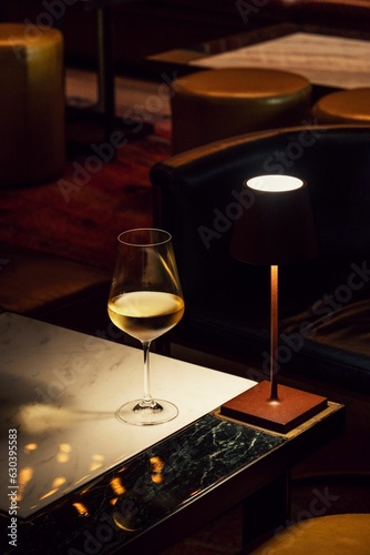 Schilderij op canvas Table lamp lit brightly on a wooden table beside a stemmed glass of white wine