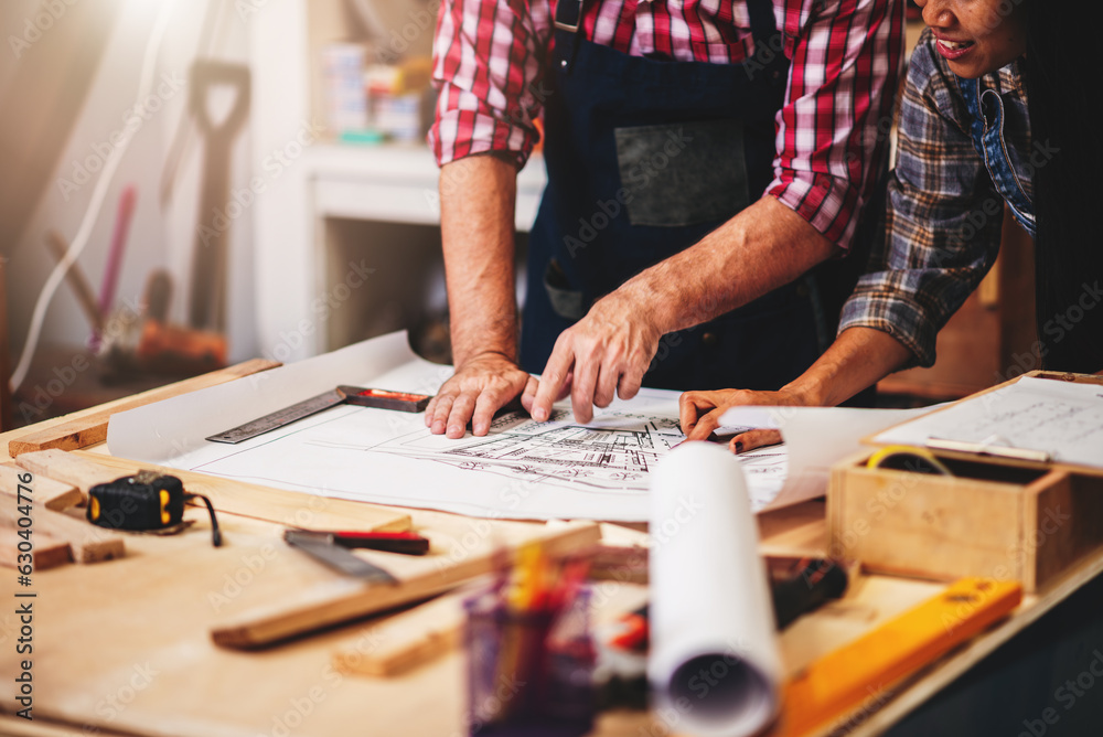 Fototapeta premium Small business furniture owner and professional architect interior designer working in carpenter workshop with blueprint and tablet discussing about home furnishing design project.