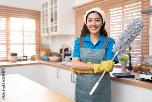 Portrait Asia woman in workwear maid cleaning home and holding dusting brush in her hand, wearing rubber gloves and apron at home	