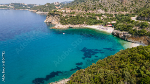 Aerial view of sea bay, sandy beach with umbrellas, trees, mountain at sunny day in summer. Blue lagoon in Syvota Greece. Tropical landscape with island, white sandy bank, blue water. Top view