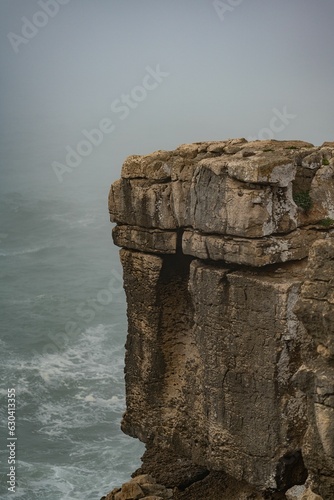 Foto Vertical shot of a rocky cliff by the sea covered in fog
