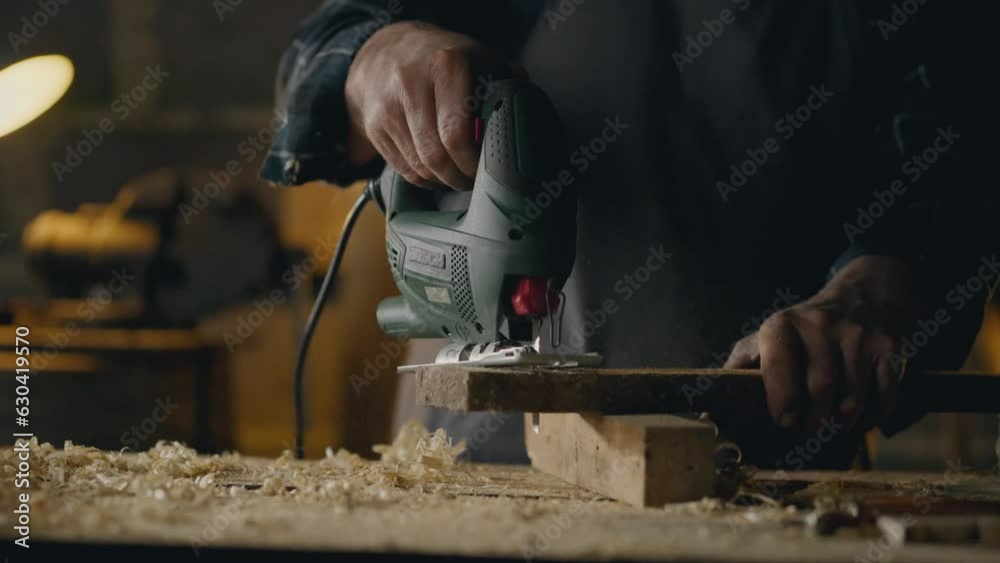Wood shavings, Workshop worker Carefully cuts a hole with an electric jigsaw with a wood saw In the workshop Follow-up shot Junior specialist Works at a carpentry table In a carpentry shop, workpiece