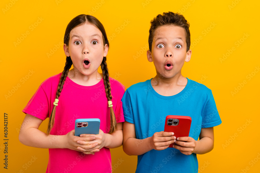 Photo of impressed funky preteen schoolchildren wear t-shirts communicating modern device isolated yellow color background Photo of impressed funky preteen schoolchildren wear t-shirts communicating modern device isolated yellow color background