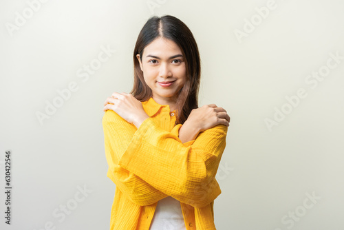 Smiling positive, hugging oneself happy asian young woman hands hug herself shoulders enjoy joyful, self hugging, self love and self care, face expression self esteem standing isolated on background.