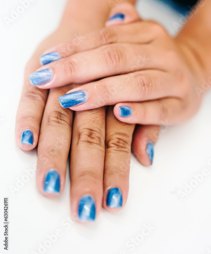 Hands of an Asian woman decorating nails with pearl blue paint.