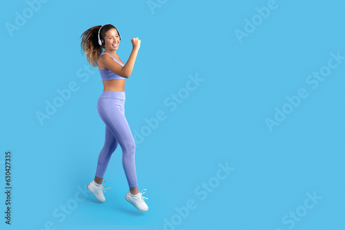 Smiling excited slim millennial european lady in sportswear, wireless headphones jump, freeze in air