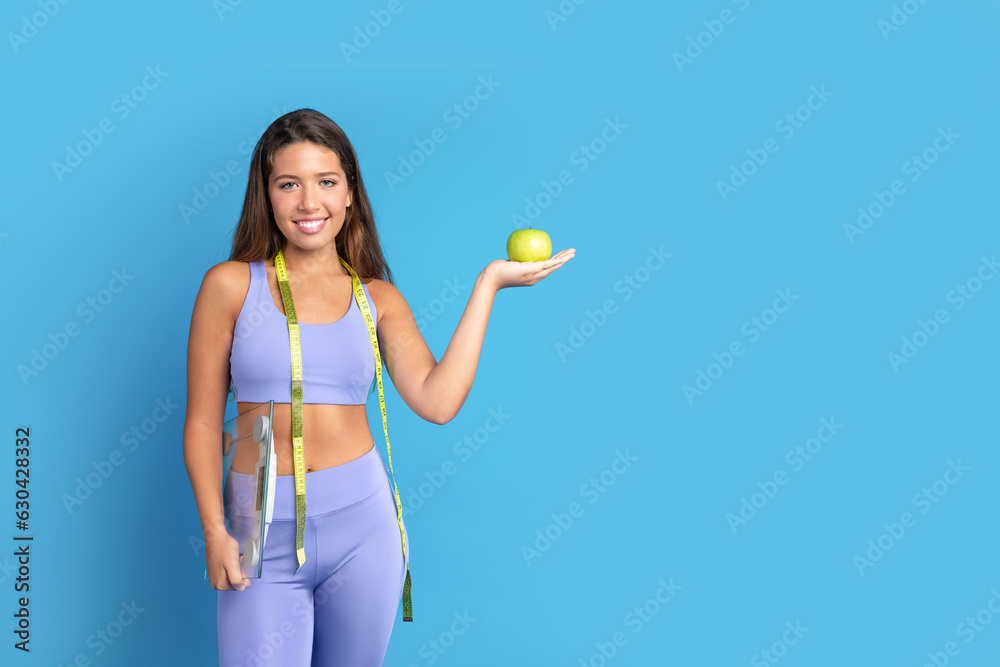 Cheerful slim young caucasian lady in sportswear with measuring tape show green apple Cheerful slim young caucasian lady in sportswear with measuring tape show green apple