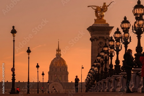 A jogger runs on the Alexandre III bridge in Paris at sunset. We see the Invalides in the background