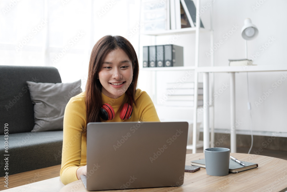 Young beautiful Asian woman using laptop computer, relaxing in her free time in the living room. Young beautiful Asian woman using laptop computer, relaxing in her free time in the living room.