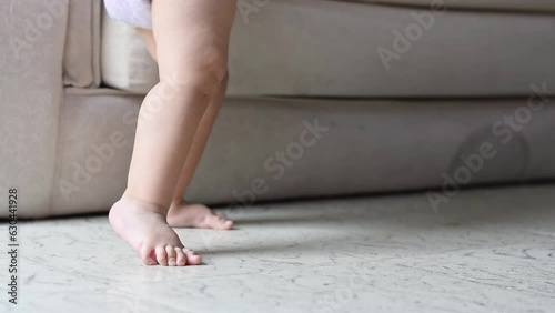 close-up of the feet of a Caucasian baby girl standing next to a sofa, learning to walk