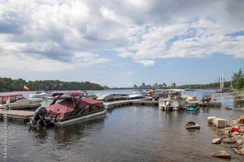 View of a dock in a marina on the Ottawa River in Gatineau, boats, dock, ramps, Gatineau in background, sunny, nobody