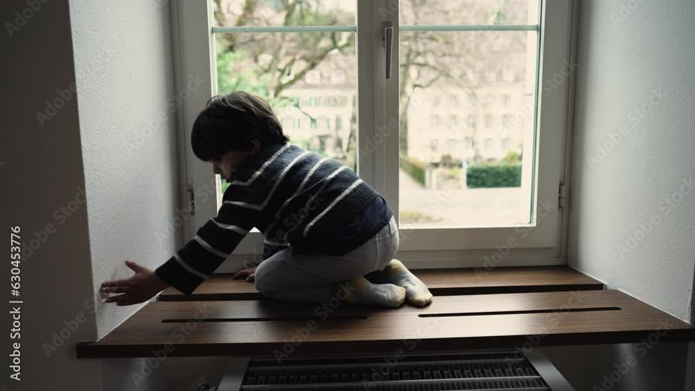 One little boy sitting by window on wooden holder near glass