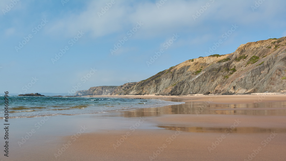 Cliffs reflecting in a tidal wave on the Praia da Bordeira, Portugal