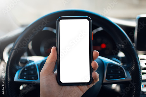 Close-up male hand holding smartphone with blank on screen against background of steering wheel of car.