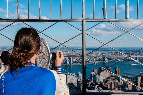 Rear view of girl looking at view of manhattan skyline with binoculars from the Empire State Building
