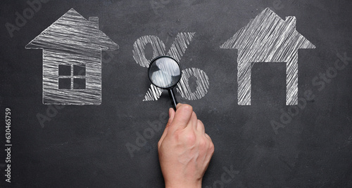 Obraz na plátně Chalk-drawn houses and a percentage sign on a blackboard, a female hand holding a magnifying glass