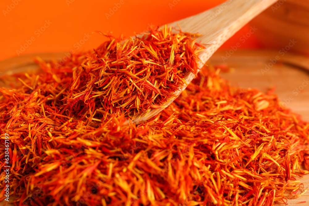 Fototapeta premium Wooden board and spoon with pile of saffron on orange background