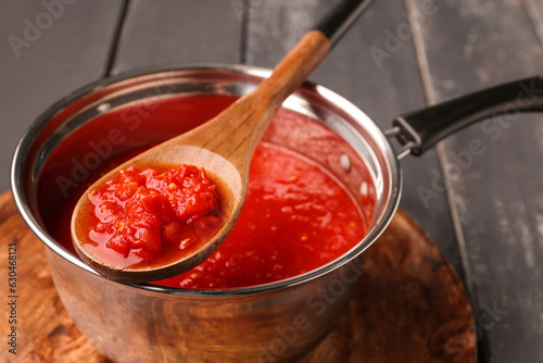 Saucepan and spoon with tasty tomato sauce on dark wooden background, closeup