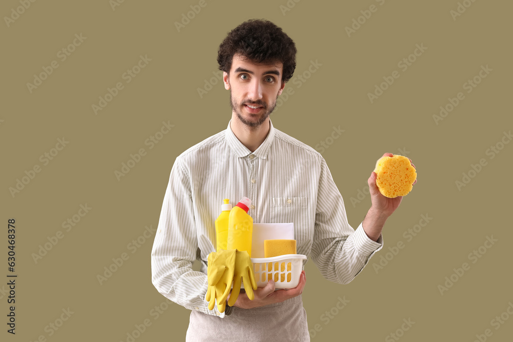 Young man with bucket of cleaning supplies on green background Young man with bucket of cleaning supplies on green background
