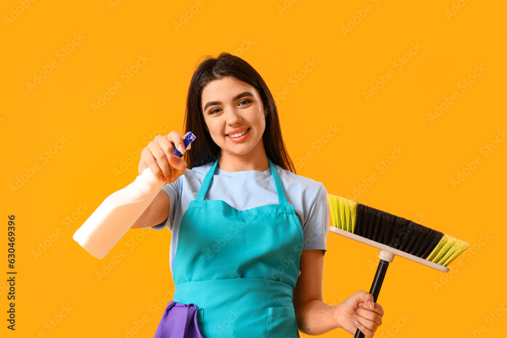 Female janitor with broom and detergent on yellow background Female janitor with broom and detergent on yellow background