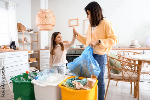 Asian mother with her little daughter sorting garbage with recycle bins in kitchen