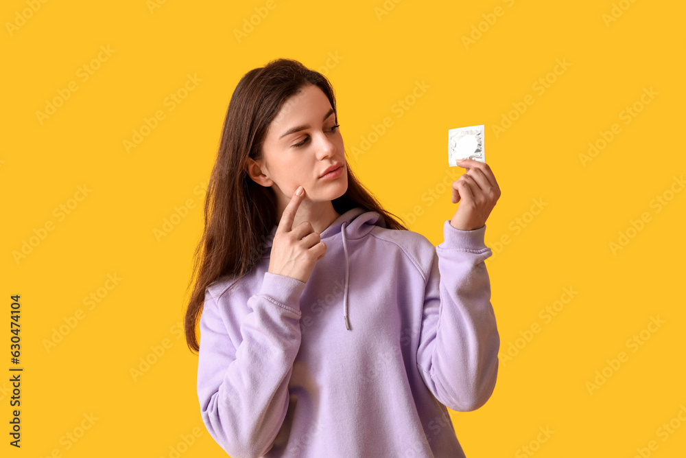 Thoughtful young woman with condom on orange background Thoughtful young woman with condom on orange background