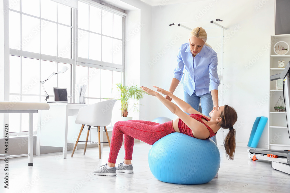 Young woman training with female physiotherapist on fitball in rehabilitation center Young woman training with female physiotherapist on fitball in rehabilitation center