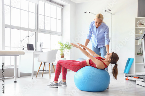 Young woman training with female physiotherapist on fitball in rehabilitation center