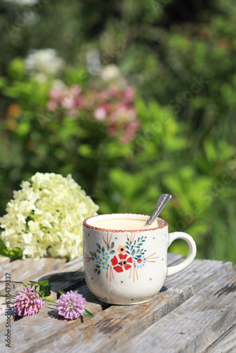 A beautiful ceramic coffee cup with flowers on the wooden table in the garden. Selective focus. 