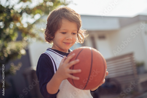 Young boy playing basketball on a basketball court outside in the suburbs