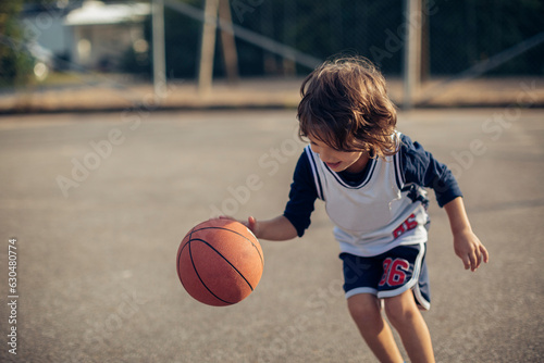 Young boy playing basketball on a basketball court outside