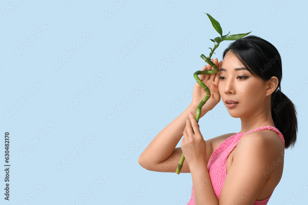Beautiful young Asian woman with healthy skin and bamboo on light blue background Beautiful young Asian woman with healthy skin and bamboo on light blue background