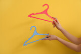 Woman holding plastic clothes hangers on yellow background