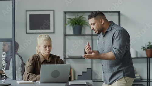 Medium shot of rude Middle Eastern man mistreating his Caucasian female subordinate at work in office