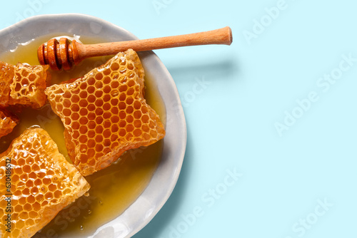 Plate with sweet honeycombs and dipper on blue background