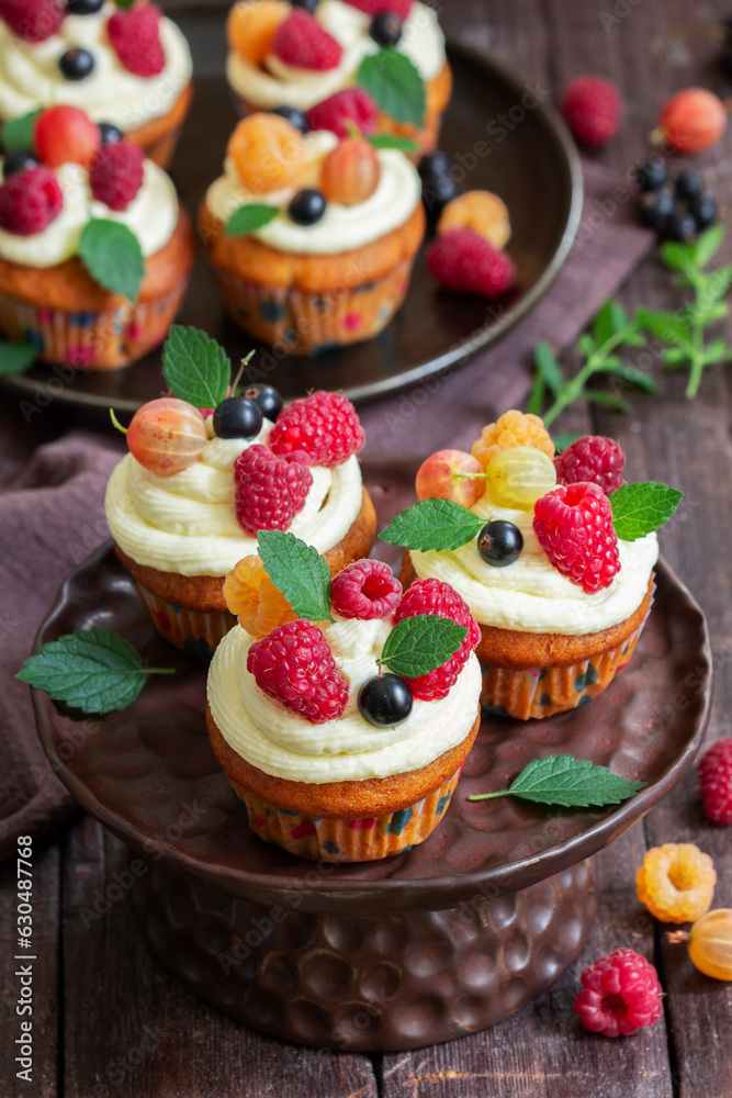 Cupcakes with butter cream and raspberry curd, decorated with berries on a wooden surface.