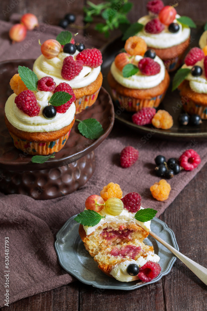 Cupcakes with butter cream and raspberry curd, decorated with berries on a wooden surface.