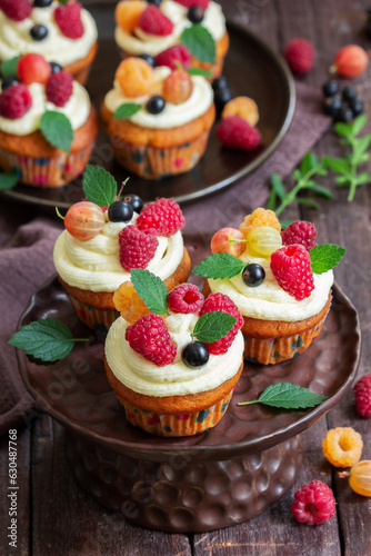 Obraz na płótnie Cupcakes with butter cream and raspberry curd, decorated with berries on a wooden surface. w salonie