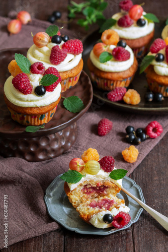 Obraz na płótnie Cupcakes with butter cream and raspberry curd, decorated with berries on a wooden surface. w salonie