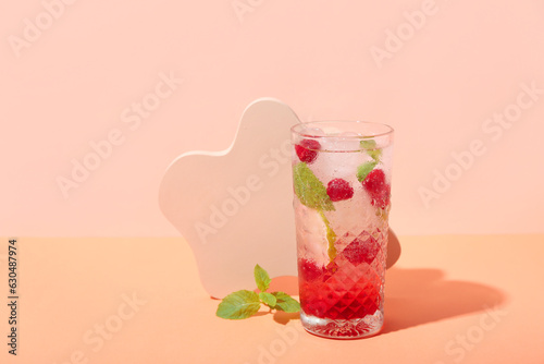 Glass of fresh raspberry mojito on pink background