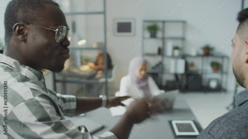 Selective focus shot of African American and Middle Eastern men standing in office defaming their female colleague
