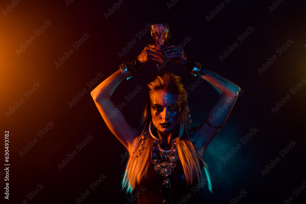 Portrait of dangerous fearless valkyrie girl hold potion cup above head orange lights isolated on dark background