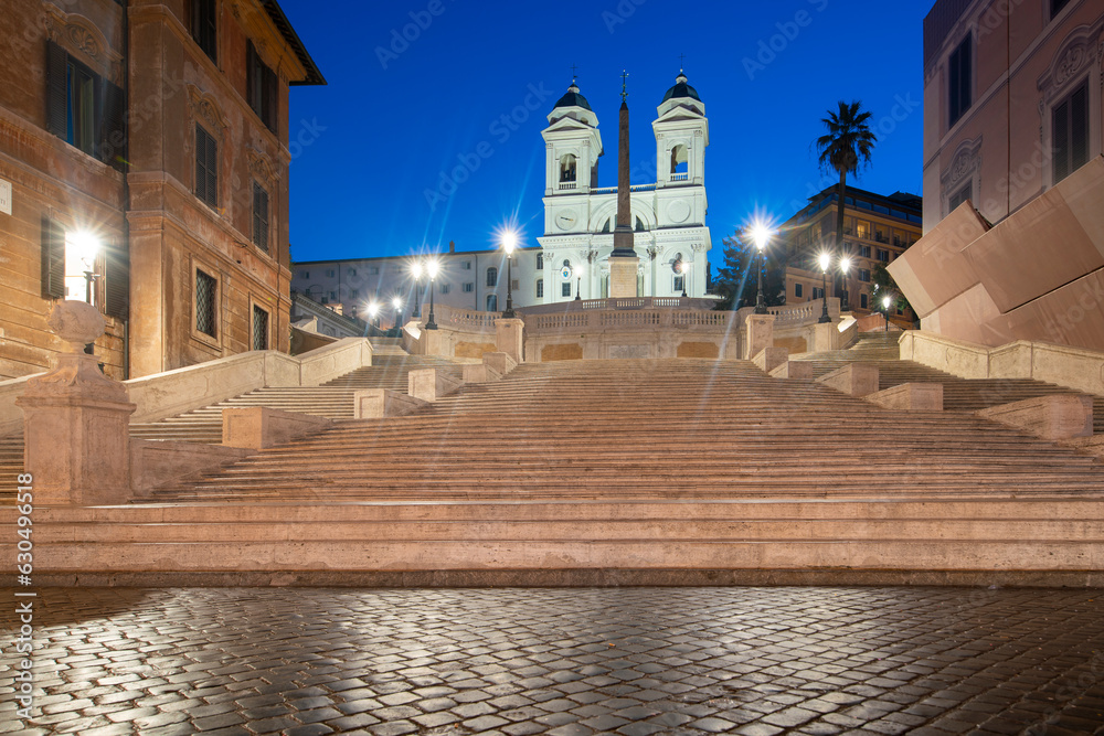 Spanish steps by sunrise in Rome with illumiinated buildings and blue sky, Italy