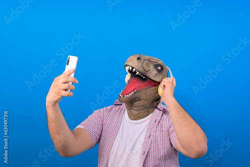 irrational man with the head of a T-Rex listens to music in his headphones on a blue background