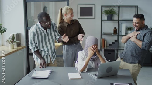 Group of three multi-ethnic colleagues making mock of their Muslim colleague at work in office