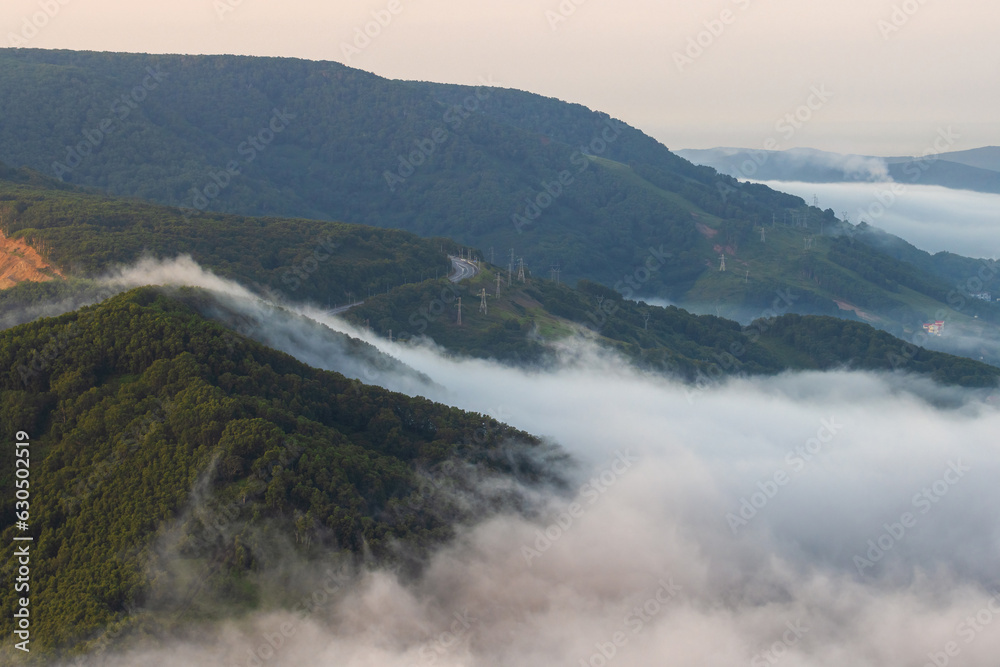 Morning foggy landscape. Fog and low clouds in the mountains. Top view of the clouds at sunrise. Beautiful aerial photograph of the hills. Road in the mountains. Kamchatka Territory, Russian Far East.
