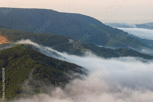 Morning foggy landscape. Fog and low clouds in the mountains. Top view of the clouds at sunrise. Beautiful aerial photograph of the hills. Road in the mountains. Kamchatka Territory, Russian Far East.